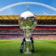 FA Trophy cup displayed on a stadium pitch with stands and arch in the background