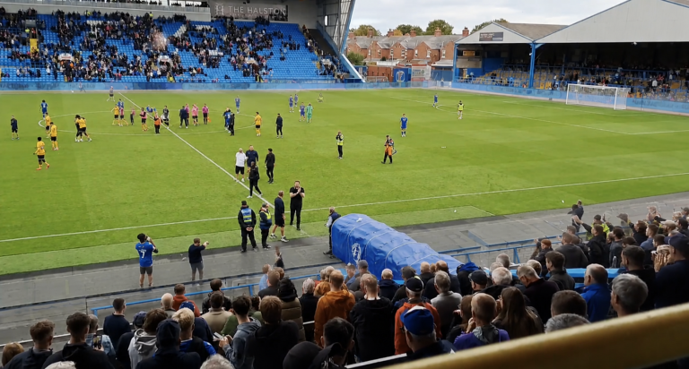 Post-match scene at Brunton Park showing Carlisle players, staff and supporters on the pitch and in the stands after a heavy defeat