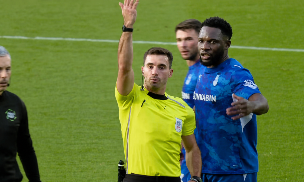 Referee raises his arm beside Oldham players during the Oldham Athletic vs Salford City match.