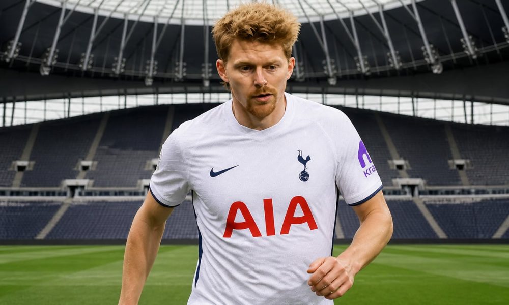 A footballer in a white Tottenham Hotspur jersey running on the pitch inside an empty stadium.