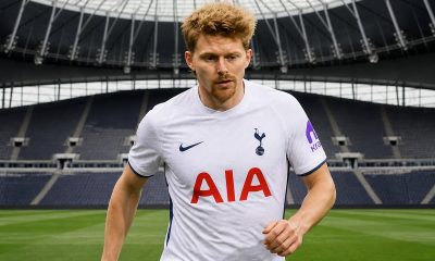 A footballer in a white Tottenham Hotspur jersey running on the pitch inside an empty stadium.