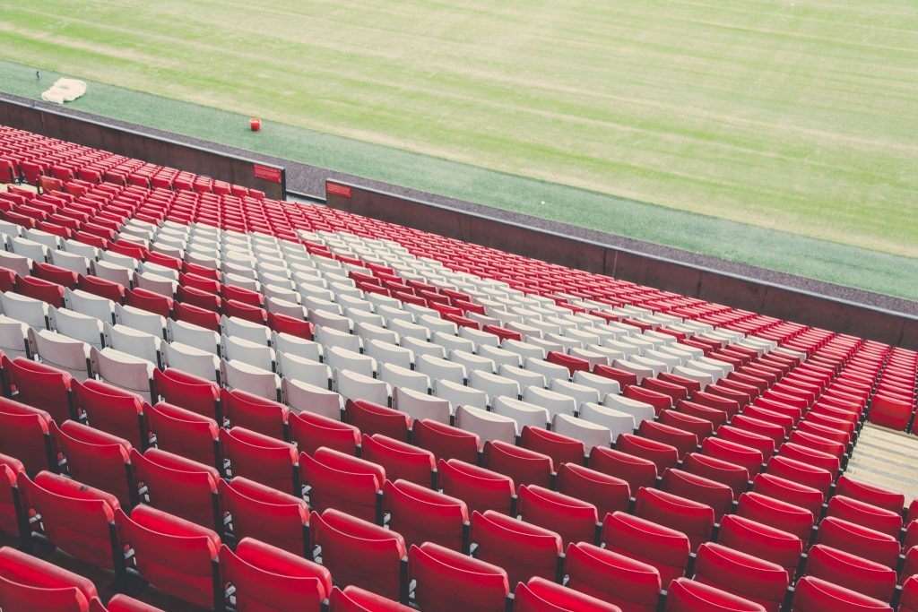 Empty red and white stadium seats beside a football pitch