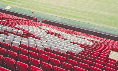 Empty red and white stadium seats beside a football pitch