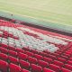 Empty red and white stadium seats beside a football pitch