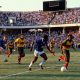 Footballers in blue and yellow kits playing in a crowded stadium